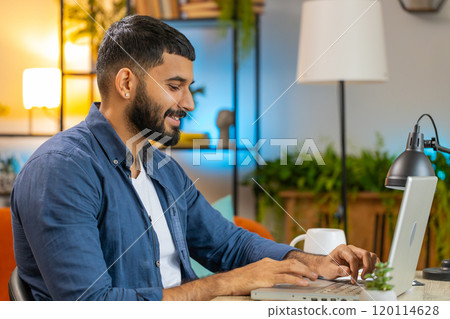 Happy Indian man freelancer typing working on laptop writing important email from home office 120114628