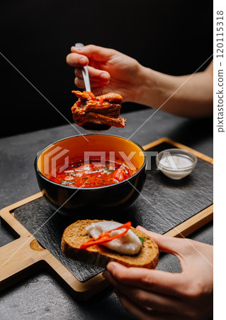 Close-up of authentic Ukrainian borscht with rye bread, sour cream, and chili pepper garnish 120115318