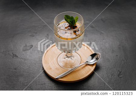 Elegant panna cotta dessert with passion fruit topping and mint in a glass on a wooden coaster Elegant panna cotta dessert with passion fruit topping and mint in a glass on a wooden coaster 120115323