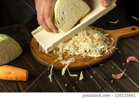 Hands skillfully slice cabbage on a wooden board, surrounded by vibrant carrots and garlic. The warm kitchen exudes a sense of comfort and seasonal abundance, perfect for hearty meals 120115691