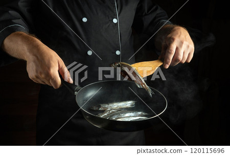 A skilled chef expertly flips fresh fish in a hot skillet, showcasing culinary techniques in a stylish kitchen. The steam and action create a vibrant cooking atmosphere 120115696