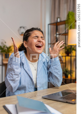 Aggressive young Indian woman screams yells from stress tension panic sitting at home office desk Aggressive young Indian woman screams yells from stress tension panic sitting at home office desk 120115705