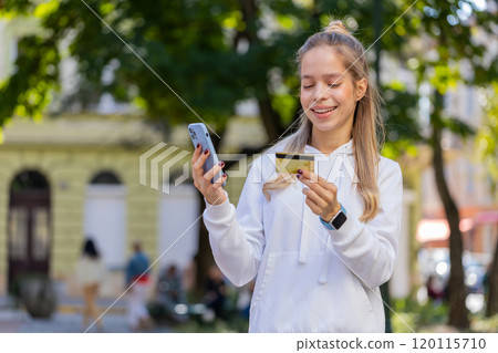 Happy young woman using credit bank card and smartphone purchases online shopping on city street Happy young woman using credit bank card and smartphone purchases online shopping on city street 120115710