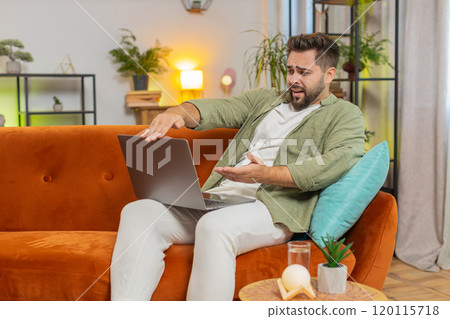 Upset young Caucasian young man sitting on sofa at home using laptop having anxiety and stress Upset young Caucasian young man sitting on sofa at home using laptop having anxiety and stress 120115718