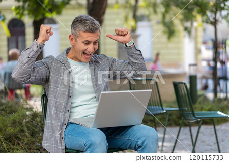 Happy man freelancer working on laptop screams in triumph win celebrating success sitting on chair 120115733