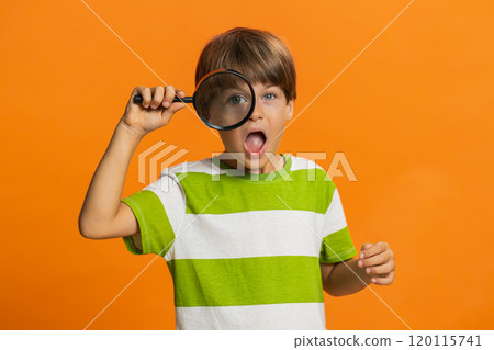 Child boy kid holds magnifying glass near face looking at camera with big zoomed eye, analyzing 120115741