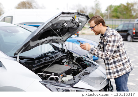 Young man checking under the hood of his car to figure out what the problem is. Young man checking under the hood of his car to figure out what the problem is. 120116317