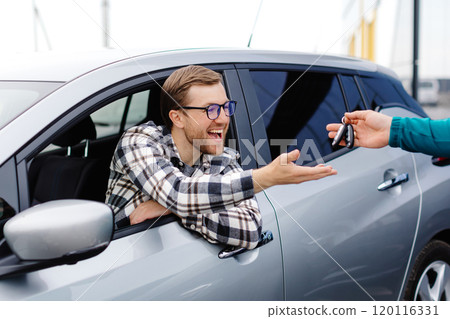 Salesman giving key to customer in modern auto dealership. Concept of choosing and buying new car at showroom Salesman giving key to customer in modern auto dealership. Concept of choosing and buying new car at showroom 120116331