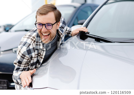 Young bearded man embracing his new car at the dealership smiling joyfully Young bearded man embracing his new car at the dealership smiling joyfully 120116509