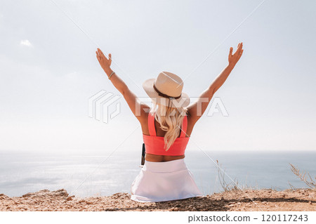A woman wearing a pink top and a straw hat is sitting on a beach, looking out at the ocean. She is smiling and she is enjoying the view. A woman wearing a pink top and a straw hat is sitting on a beach, looking out at the ocean. She is smiling and she is enjoying the view. 120117243