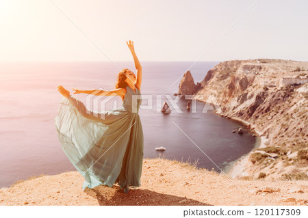 Woman green dress sea. Female dancer posing on a rocky outcrop high above the sea. Girl on the nature on blue sky background. Fashion photo. Woman green dress sea. Female dancer posing on a rocky outcrop high above the sea. Girl on the nature on blue sky background. Fashion photo. 120117309