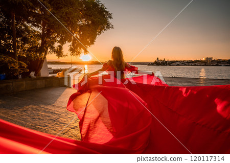 Sunrise red dress. A woman in a long red dress against the backdrop of sunrise, bright golden light of the sun's rays. The concept of femininity, harmony. 120117314