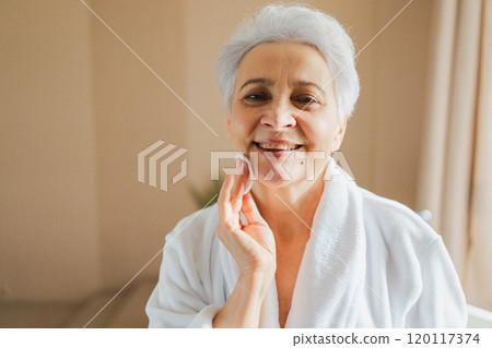 Mature adult old woman doing daily beauty routine removing makeup with cotton pad. Senior woman with lotion sponge washing face gets facial treatment. Skin care aging beauty skincare cleansing 120117374
