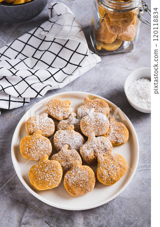 Homemade pumpkin shaped cookies in powdered sugar on a plate on a table vertical view Homemade pumpkin shaped cookies in powdered sugar on a plate on a table vertical view 120118834