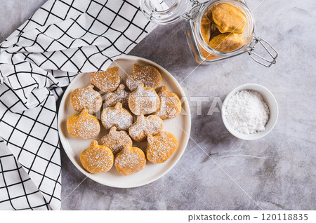 Sweet pumpkin cookies in powdered sugar on a plate on the table top view Sweet pumpkin cookies in powdered sugar on a plate on the table top view 120118835