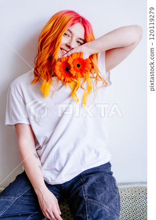 Portrait of young Caucasian woman with colorful hair holding orange flowers, smiling and joy. Casual clothing, playful and cheerful mood. Youthfulness, happiness, self-expression in modern lifestyle. Portrait of young Caucasian woman with colorful hair holding orange flowers, smiling and joy. Casual clothing, playful and cheerful mood. Youthfulness, happiness, self-expression in modern lifestyle. 120119279
