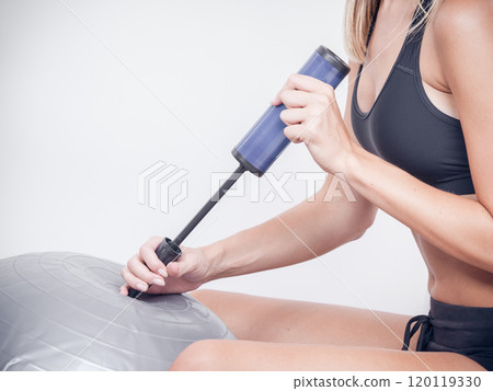Fitness woman with air pump inflating fit ball 120119330