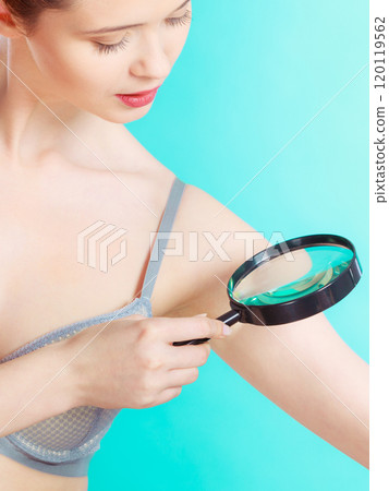 Woman using magnifying glass to examine her moles skin 120119562