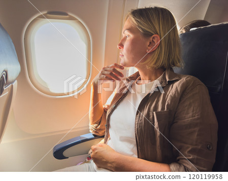 Passenger woman is flying in plane. Girl sitting in airplane looking out window going on trip vacation travel. Traveling female inside plane enjoying flight. Traveling girl 120119958