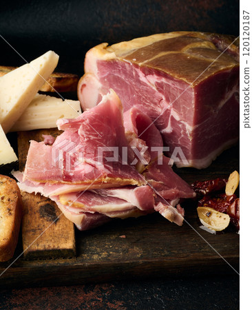 A piece of prosciutto, slices of ciabatta and cheese on a wooden board 120120187