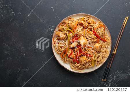 Asian udon noodles with chicken and vegetables sprinkled with sesame seeds on dark background top view 120120357