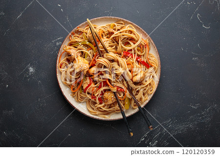 Asian udon noodles with chicken and vegetables sprinkled with sesame seeds on dark background top view 120120359