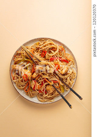 Asian chicken noodles with vegetables and chopsticks on beige background top view 120120370