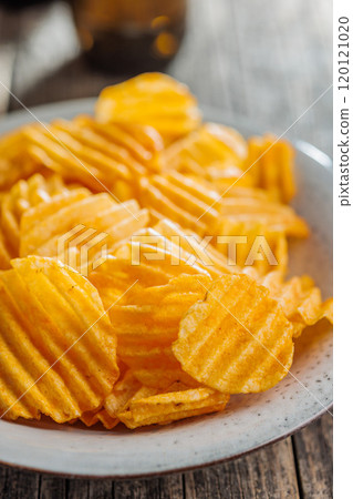 Crispy potato chips on plate on wooden table. Crispy potato chips on plate on wooden table. 120121020