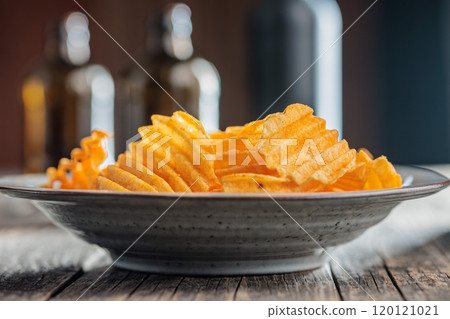 Crispy potato chips on plate on wooden table. Crispy potato chips on plate on wooden table. 120121021