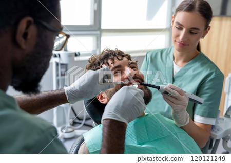 Orthodontist conducting dental checkup in modern clinic examining patient's teeth 120121249