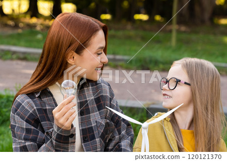 Little girl and teacher exploring wind turbine in park learning about eco-friendly energy 120121370