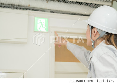 一名身穿消防設備工作服的婦女檢查疏散導燈 一名身穿消防設備工作服的婦女檢查疏散導燈 120121579