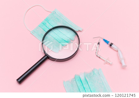 Broken Medical Syringe and Green Torn Medical Face Mask with Magnifying Glass 120121745