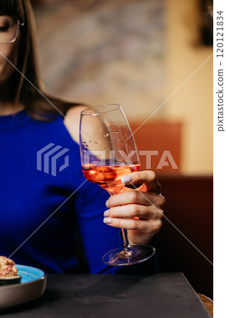 Close up of womans hand holding a glass of rose wine, showcasing elegance and relaxation Close up of womans hand holding a glass of rose wine, showcasing elegance and relaxation 120121834