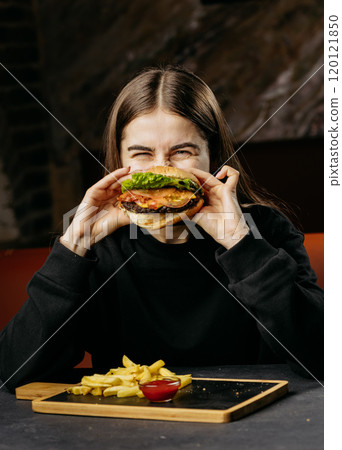 Excited woman holding a juicy burger with fresh toppings, capturing the joy of indulgent dining 120121850