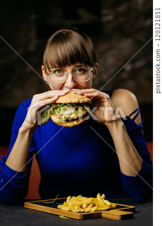 Woman enjoying a big bite of a gourmet burger with fresh greens, savoring each delicious flavor 120121851