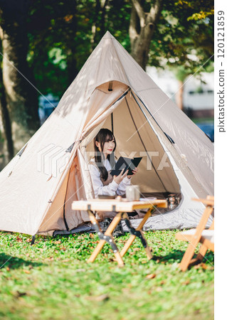Young woman enjoying reading in a tent 120121859