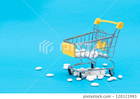Scattered Pills or Capsules and Shopping Cart on Blue Background Scattered Pills or Capsules and Shopping Cart on Blue Background 120121993