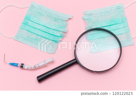 Broken Medical Syringe and Green Torn Medical Face Mask with Magnifying Glass 120122023