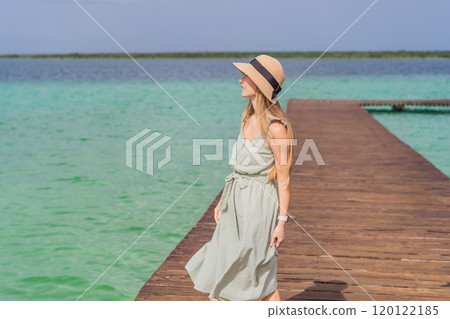 Female tourist in a turquoise dress standing on a wooden pier over the turquoise waters of Bacalar Lake, Mexico. Peaceful tropical travel destination concept 120122185