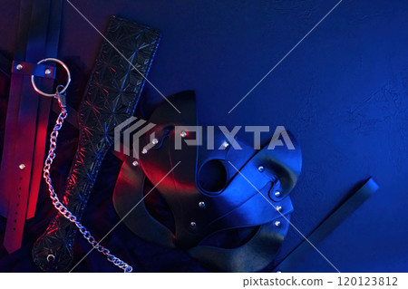 Black leather mask, collar, handcuffs, choker on black background with red and blue light, top view. Adult game props Black leather mask, collar, handcuffs, choker on black background with red and blue light, top view. Adult game props 120123812