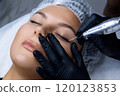 A beautician does permanent eyeliner makeup on a woman. Tattooing in a beauty salon. 120123853