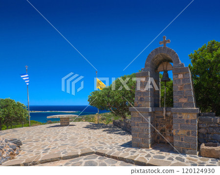 The bell tower of a chapel and the Greek flag, the double-headed eagle flag, fluttering in the sea breeze (Korokita, Crete, Greece) 120124930