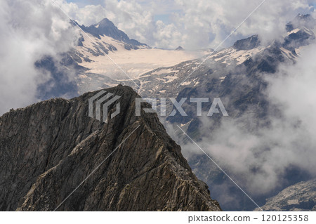 Jagged Mountain Ridge with Snow-Capped Peaks and Misty Clouds 120125358