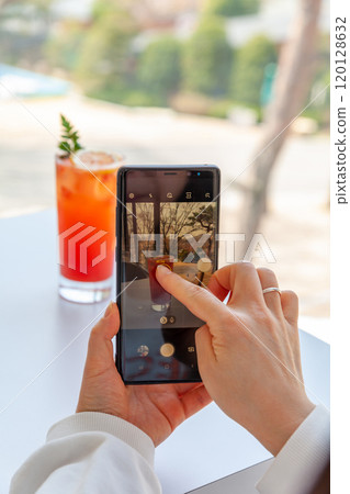A woman is filming a grapefruit ade on a table with her cell phone A woman is filming a grapefruit ade on a table with her cell phone 120128632