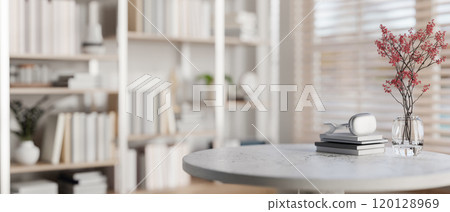 A space for displaying products on a round table with a large bookshelf in the background. 120128969