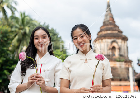 Two beautiful Asian women are holding pink lotuses and smiling at the camera. Two beautiful Asian women are holding pink lotuses and smiling at the camera. 120129365