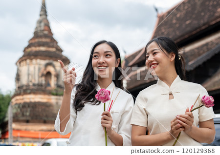Two beautiful, smiling Asian women stand in a temple, enjoying a conversation together. 120129368