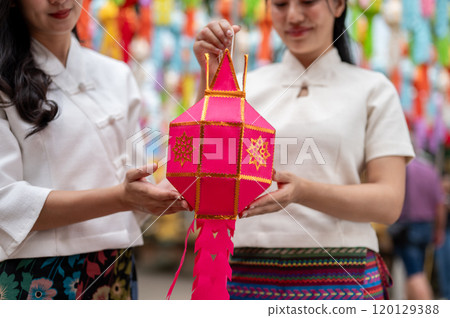 A close-up of two charming Asian women in traditional dresses hold a lantern together. 120129388