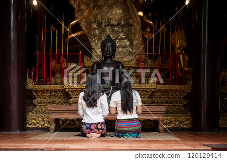 A back view of two beautiful Asian women in traditional dresses sitting in a temple, making wishes. 120129414